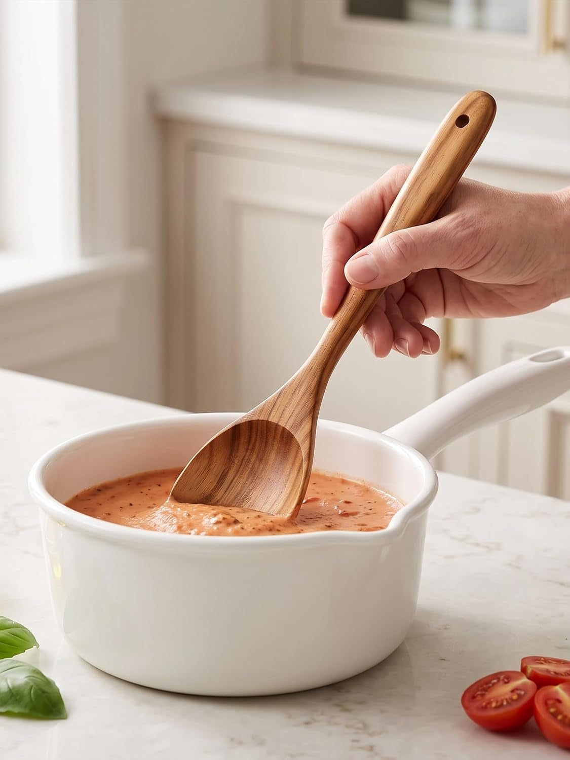 Teak spoon stirring tomato sauce in a white saucepan