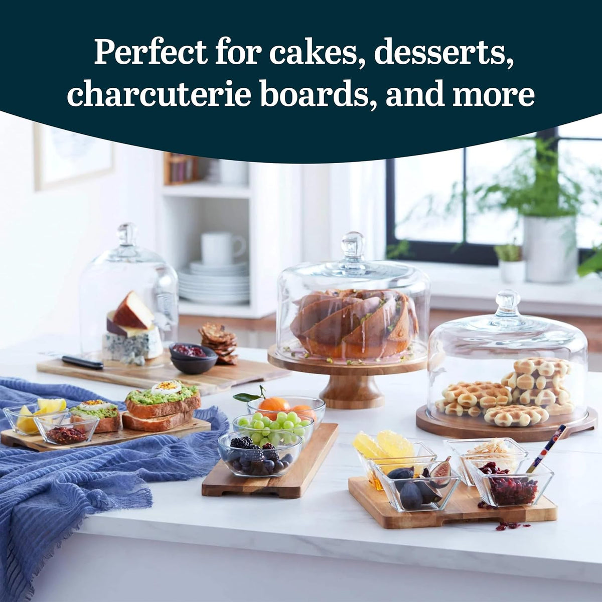 Acacia wood cake stand with glass dome on a table with desserts and snack boards