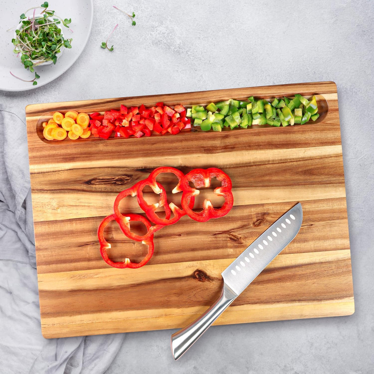 Acacia board from above with chopped peppers in the long holder and a knife beside sliced pepper