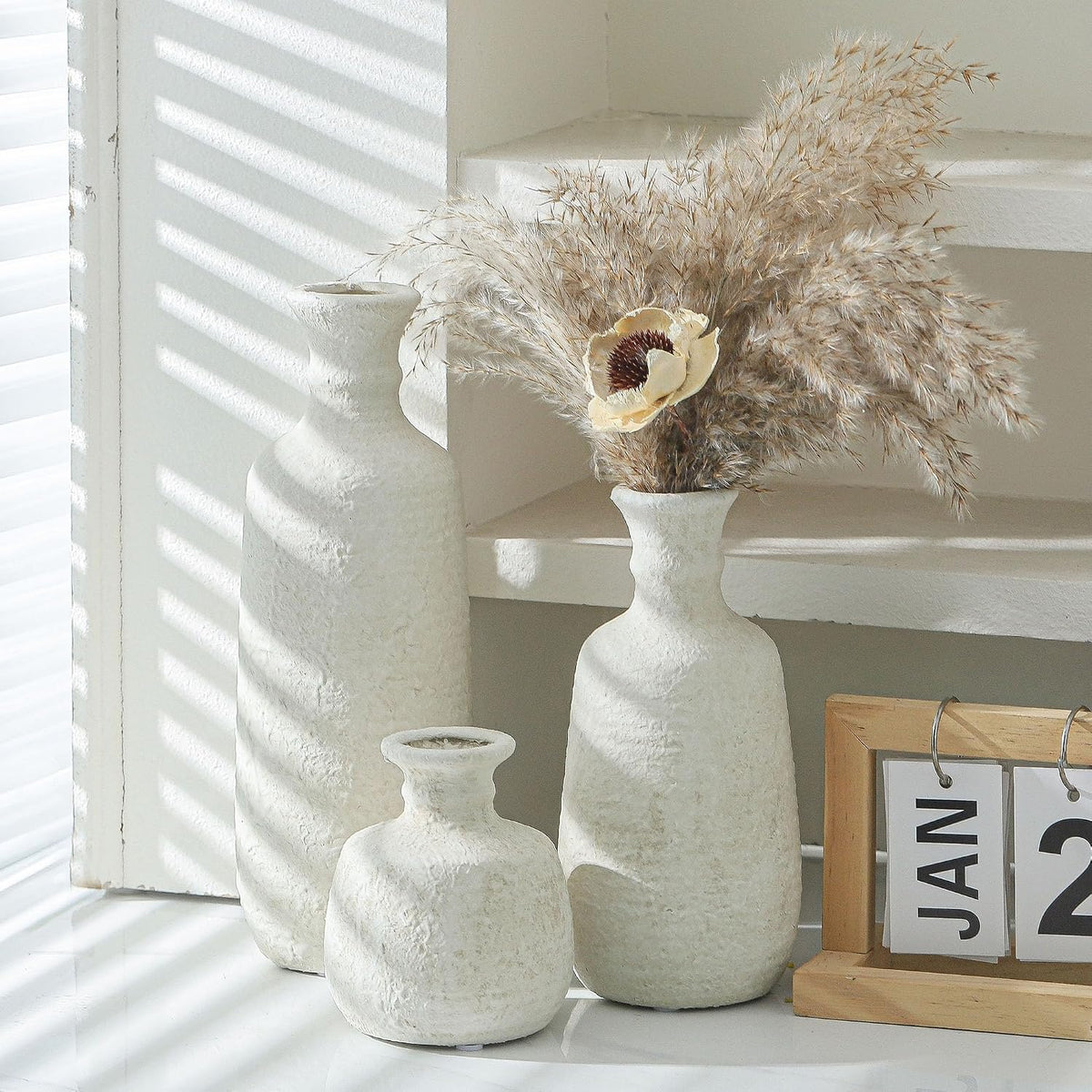 White ceramic vases with dried pampas on a sunlit shelf
