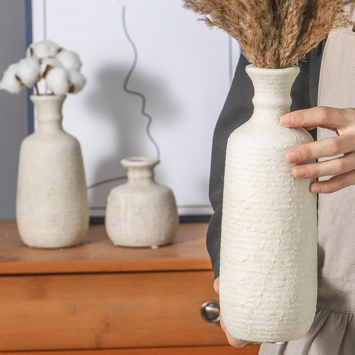 Hand placing the tallest white ceramic vase on a cabinet