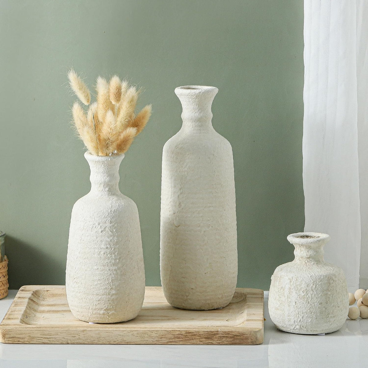 Three white ceramic vases against a green wall