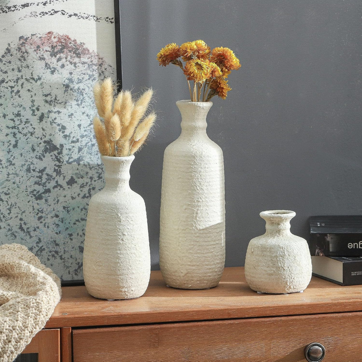 White ceramic vases with dried flowers on a wooden cabinet