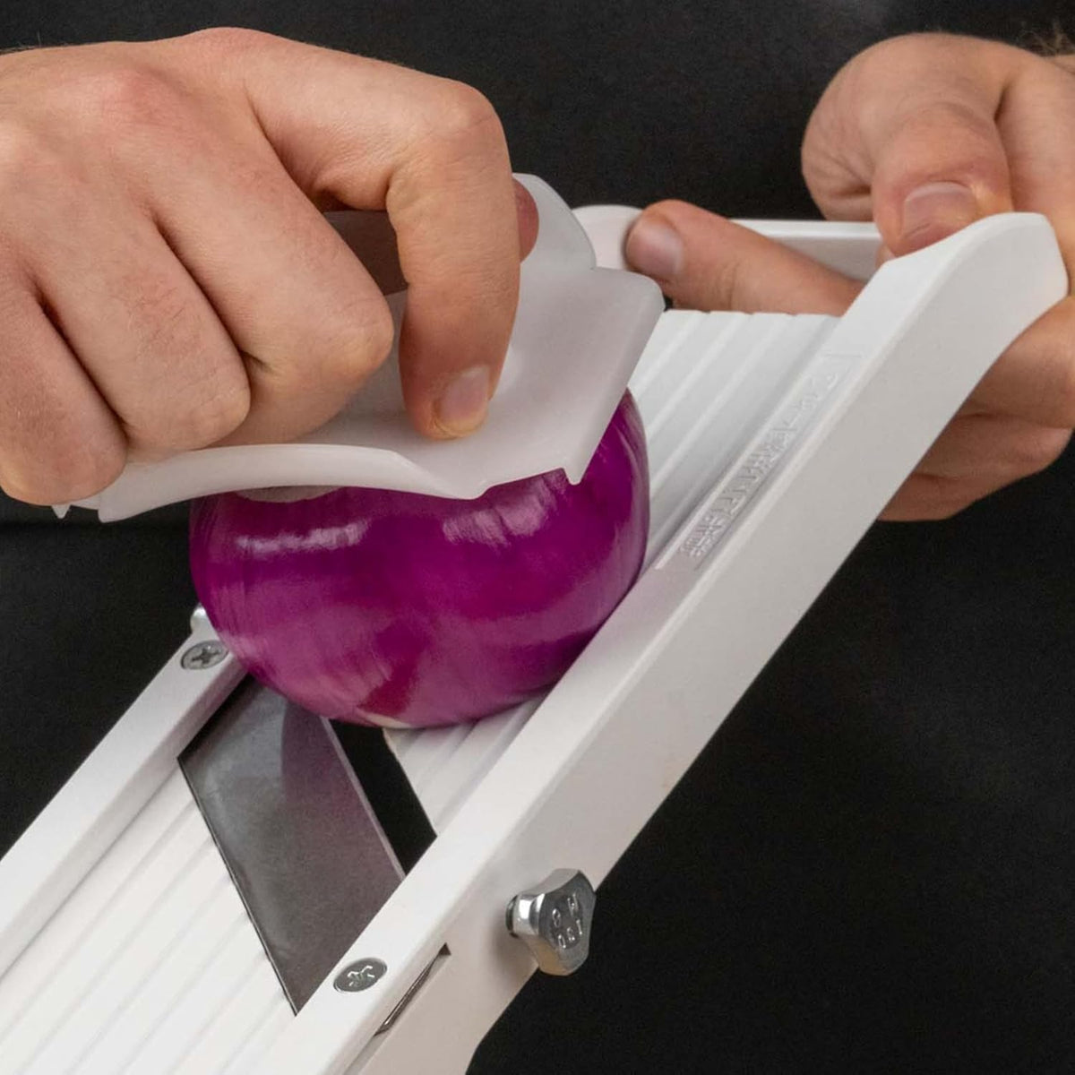Slicing a red onion on the mandoline with the safety guard