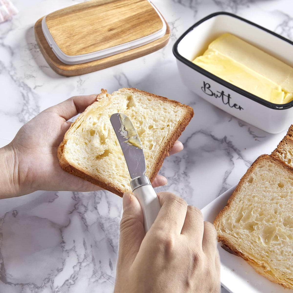 Hands spreading butter on bread beside the white butter dish