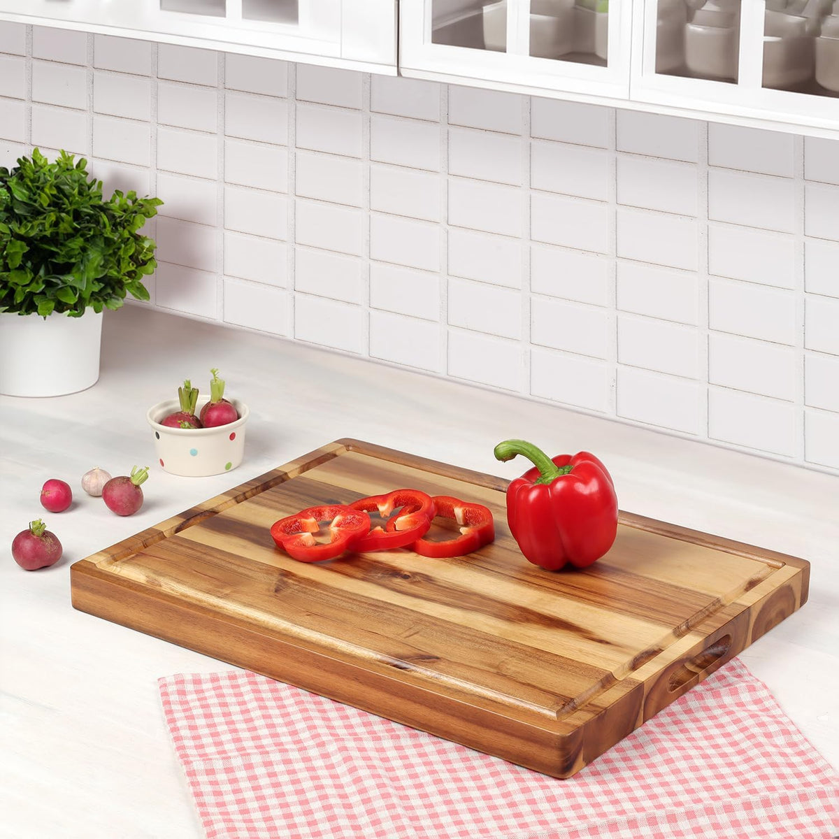 Acacia cutting board on a kitchen counter with a red pepper and sliced pepper