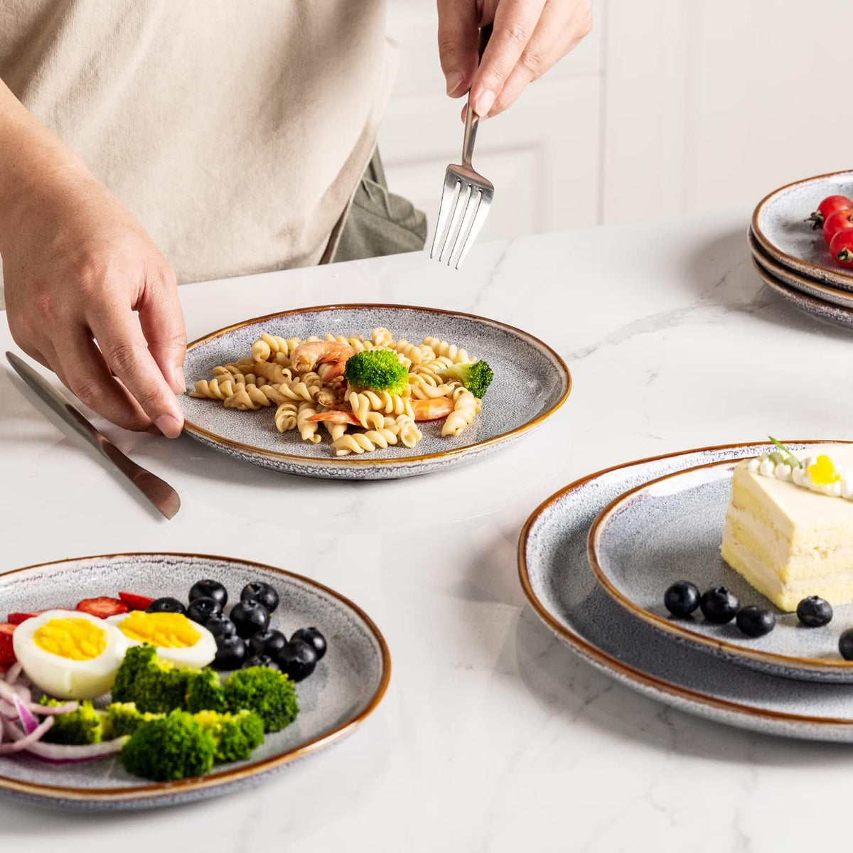 Reactive-glaze plates on a marble table with pasta, salad and cake