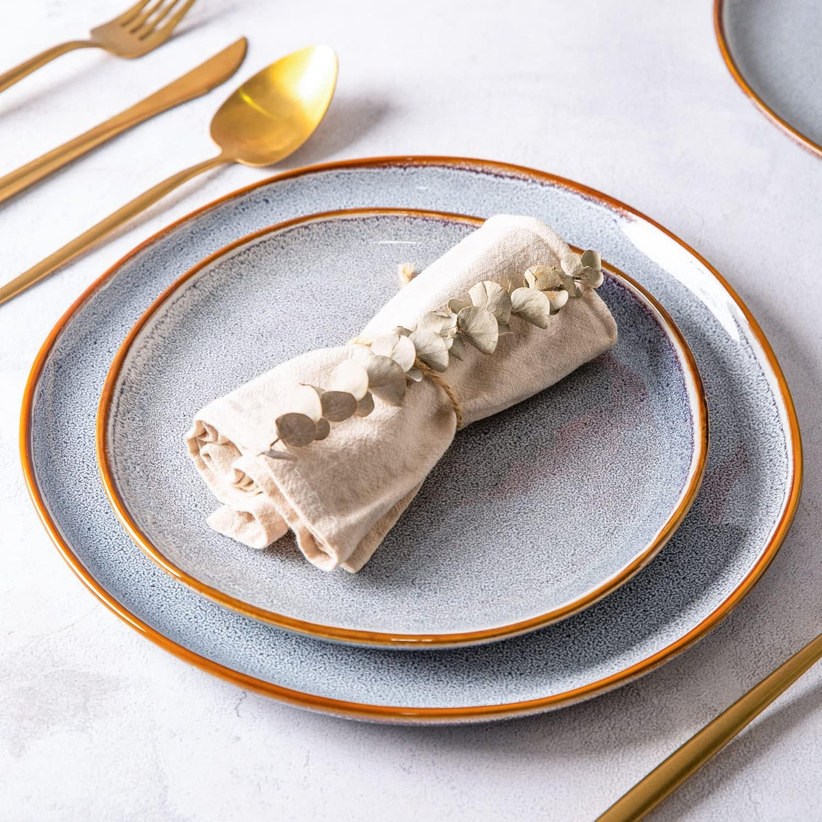 Place setting with a blue reactive-glaze plate, a linen napkin and gold flatware