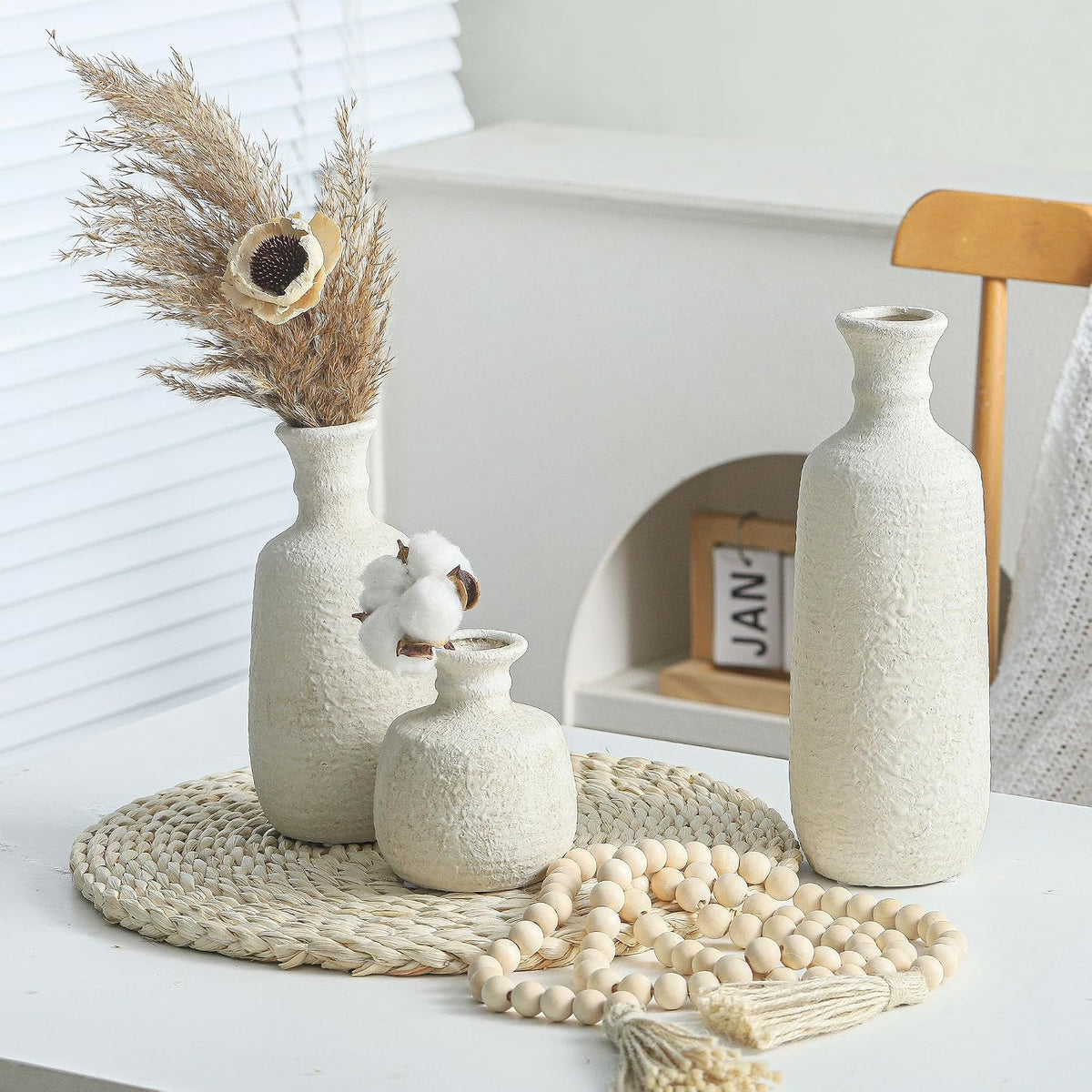 White ceramic vases with pampas and wooden beads on a table