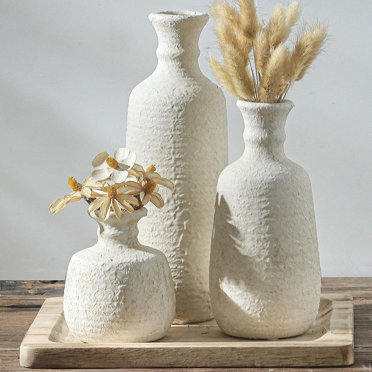 Three white ceramic vases on a wooden tray with dried stems
